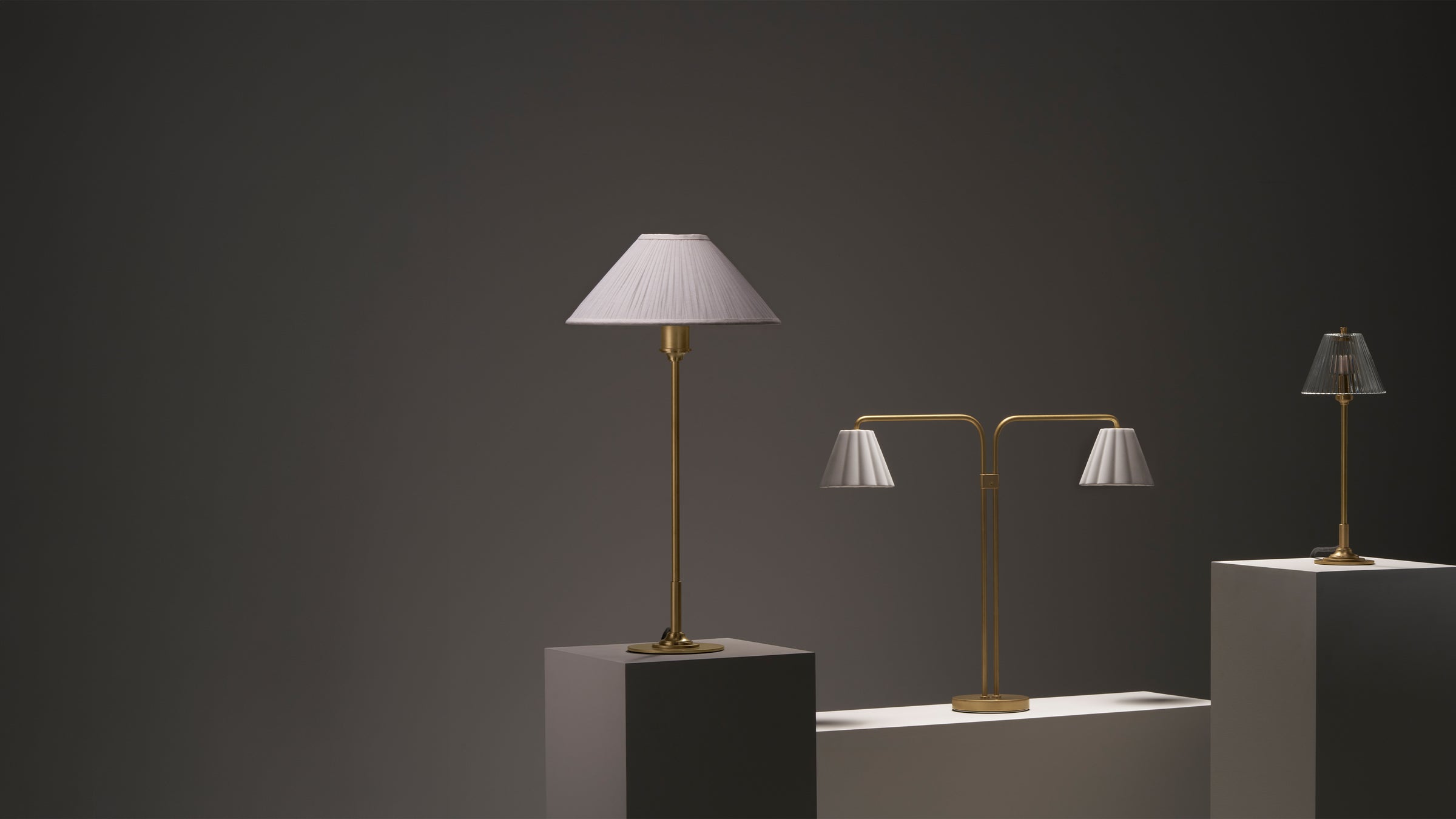 Three brass table lamps on pedestals against a dark background