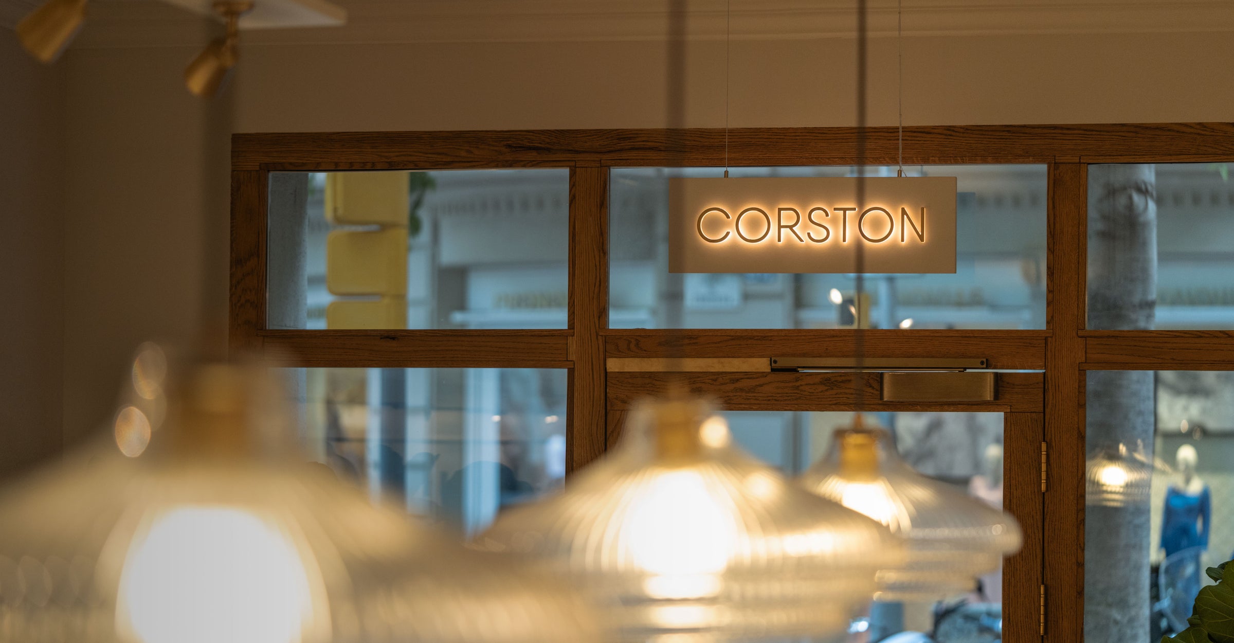 Glass door with 'Corston' sign and blurred interior lights