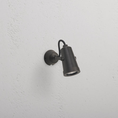Cambridge Wall Spotlight 24V in bronze, cylindrical outdoor spotlight mounted on a white textured wall.